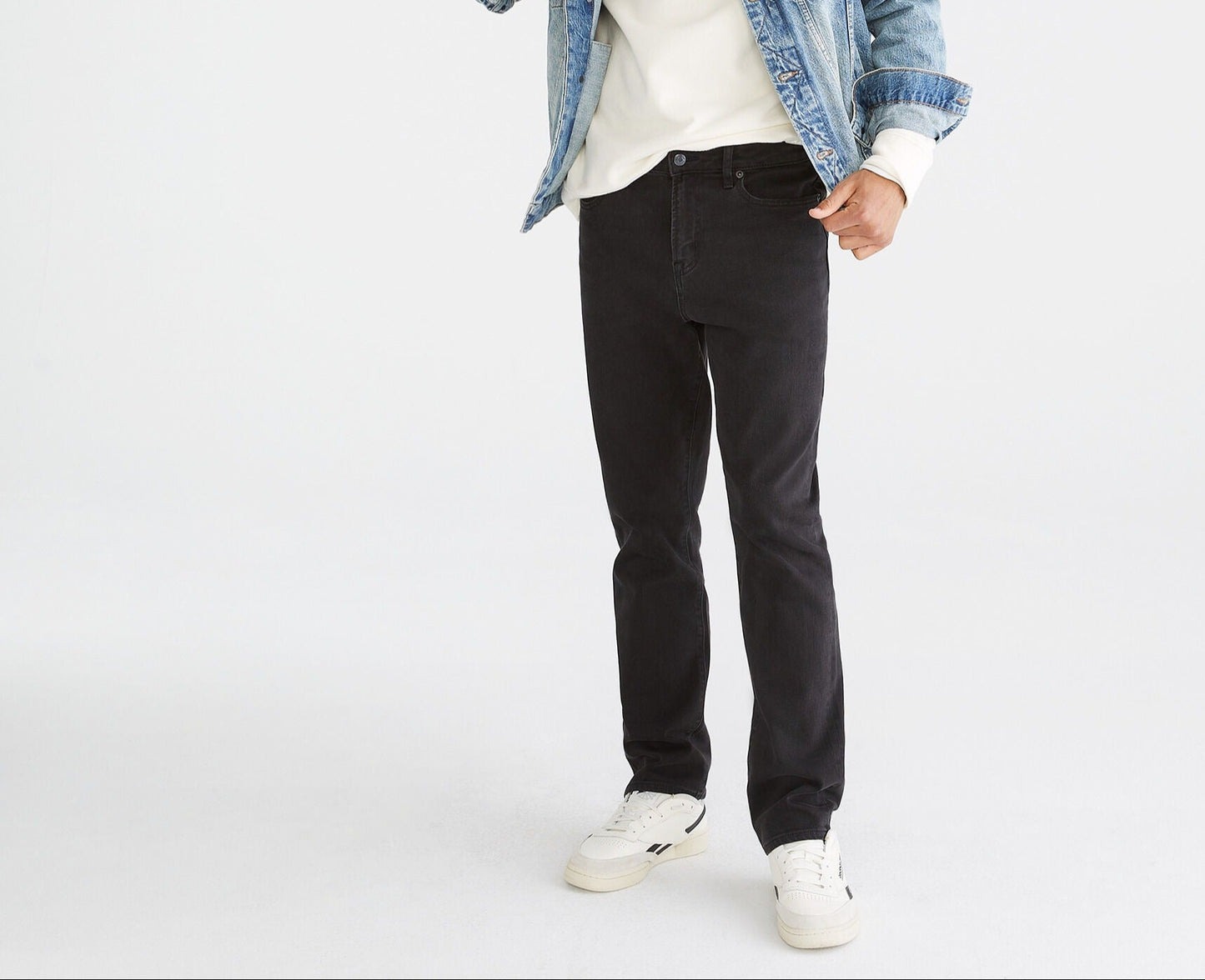 Man wearing a denim jacket, white t-shirt, black jeans, and white sneakers on a white background