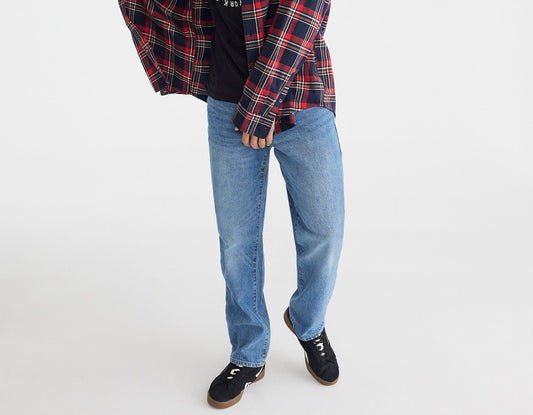 Person wearing a plaid shirt over a graphic t-shirt with jeans and black shoes on a white background