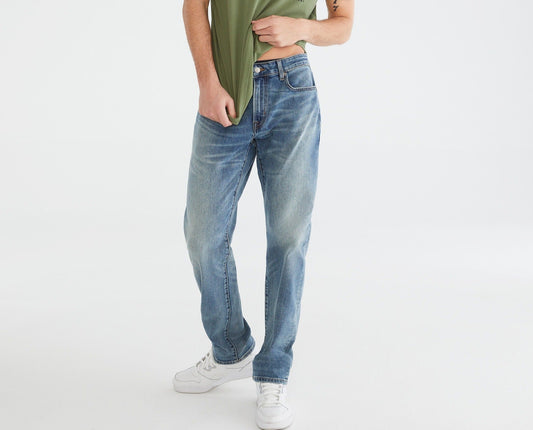 Man wearing a green t-shirt with text and blue jeans on a white background