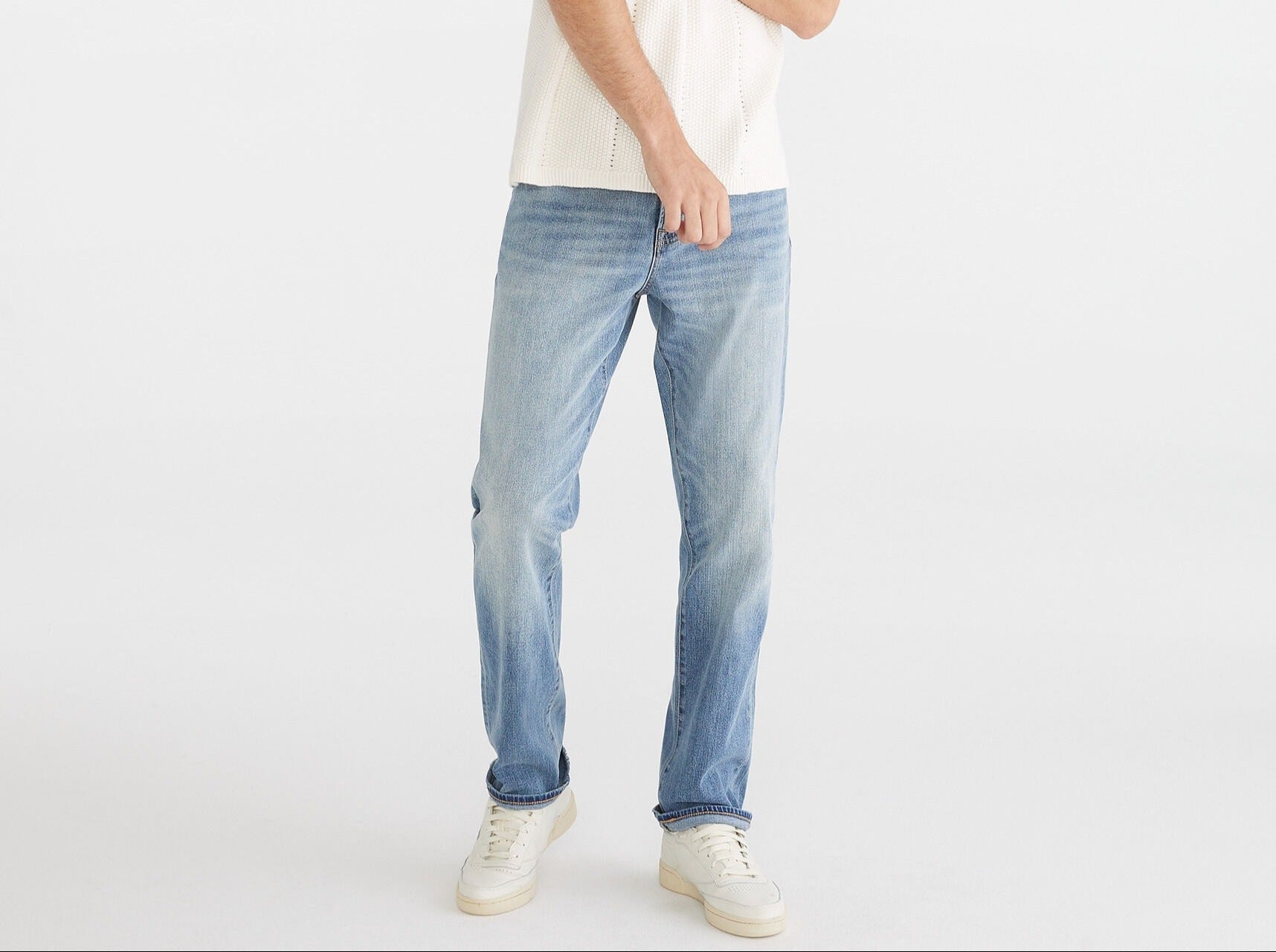 Man wearing a white polo shirt and light blue jeans on a white background