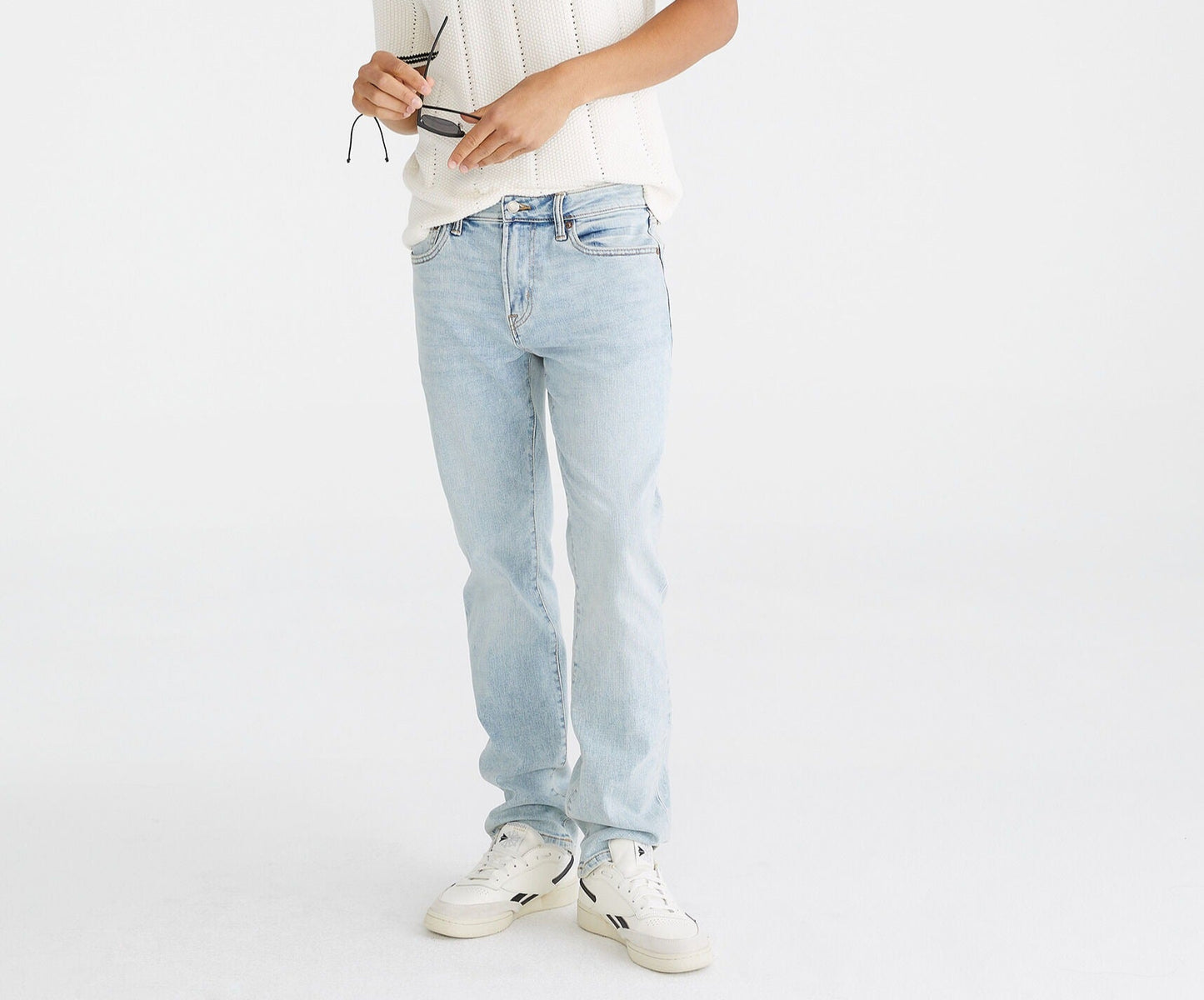 Person wearing a white polo shirt and light blue jeans on a white background
