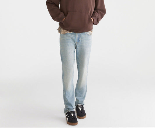Person wearing a brown hoodie, light blue jeans, and a green cap on a white background